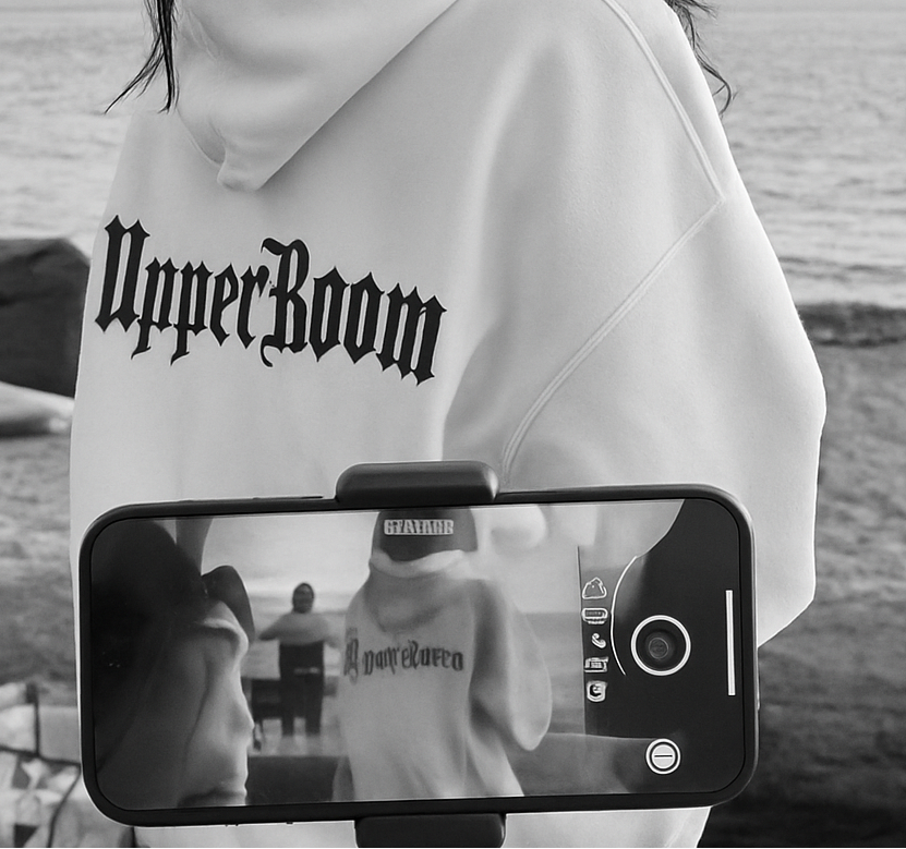 Person wearing a white hoodie with 'Upper Room' branding, standing on a beach.